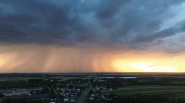 Gün batımında fırtına bulutları altında huzurlu bir köy.