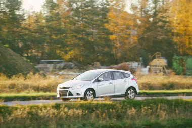 Kırsal yolda beyaz hibrit araba sürüyor.