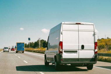 Kırsal yol boyunca ilerleyen beyaz minibüs
