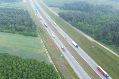 Kırsal otoyolda yarı kamyon çevresi yeşillikle çevrili.