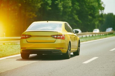 Sarı araba ormanın yanından geçiyor.