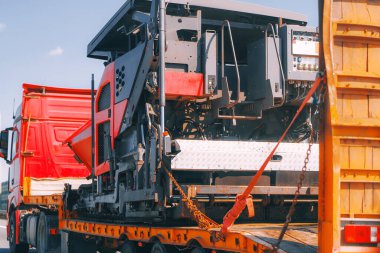 Otoyolda inşaat makineleri taşıyan kırmızı kamyon.