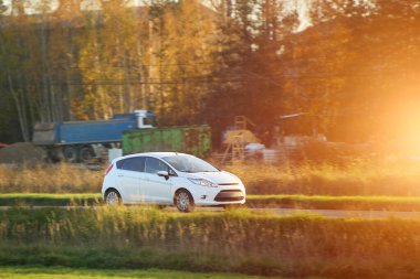 Akşamleyin kır yolundan geçen beyaz bir araç.