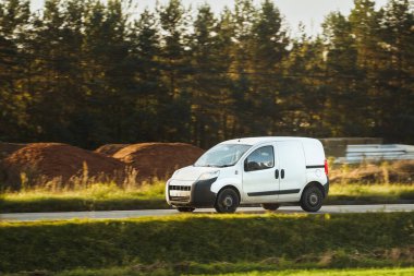 Kırsal yolda yeşil manzaralı hızlı beyaz minibüs.