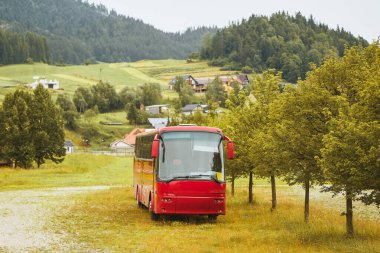 Kırsal evlerin ve tepelerin yakınında kırmızı otobüsü olan yeşil kırsal bölge.