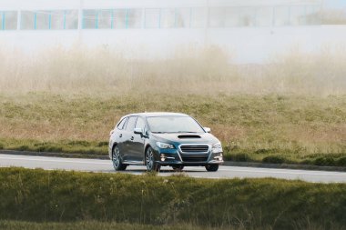 Çimenli arka plan ve modern bina ile yoldaki mavi spor arabanın ön görüntüsü