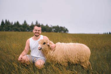 Beyaz atletli bir adam dışarıda koyun besliyor.