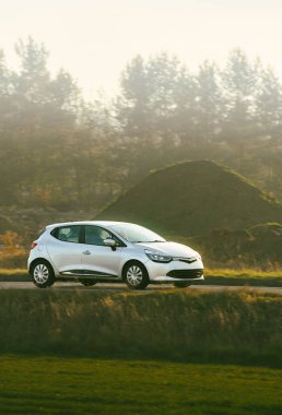 Yeşil ağaçların yanında beyaz araba sürüyor.