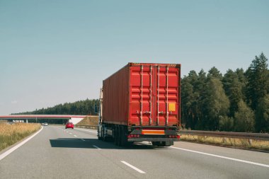 Kırmızı kamyon açık yolda kargo taşıyor.