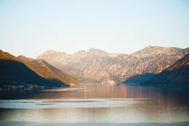 Yumuşak güneş ışığı, Kotor Körfezi 'nin sakin sularıyla buluşan engebeli dağ yamaçlarını aydınlatarak, Karadağ' da sakin ve resimli bir manzara yaratıyor