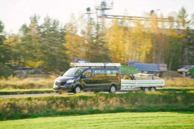 Kırsal yolda siyah minibüs römork çekiyor.