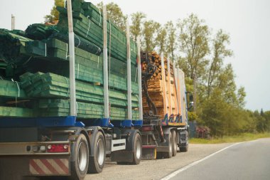Kereste ve kalas taşıyan kamyonlar kırsal yolda ilerliyor.