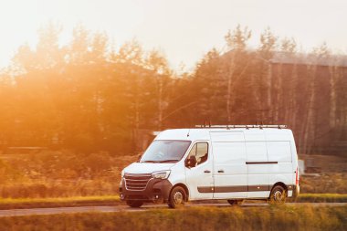 Kırsal yolda beyaz minibüs sürüyor.