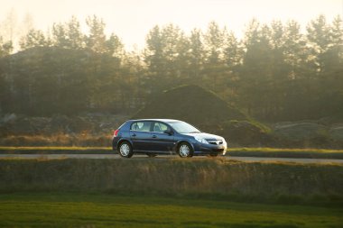 Siyah hatchback arabası şehir caddesinde geziniyor.