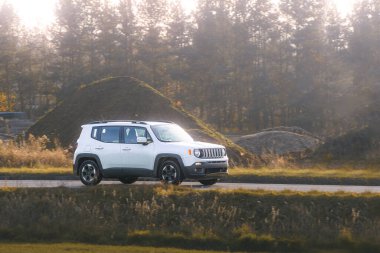 Parlak sonbahar yeşillikleri ve ormanlarla çevrili asfalt bir köy yolunda hızla ilerleyen bir SUV.