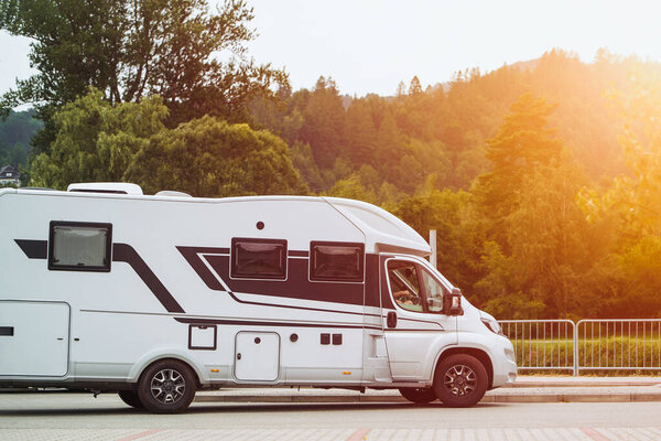 Белый фургон для кемпинга припаркован возле деревьев в живописной местности