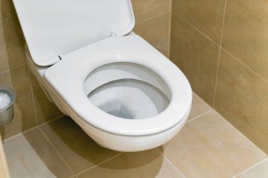 Bej kiremitli banyo ve duvara monte edilmiş tuvalet.