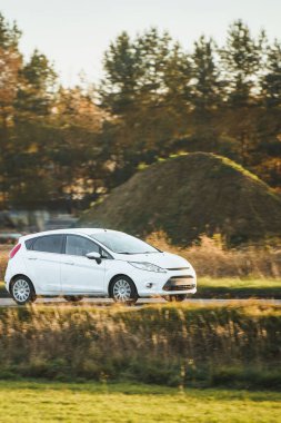 Beyaz araç sonbahar kırsalından geçiyor.