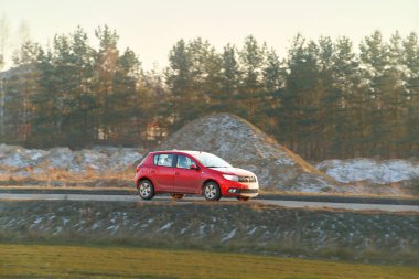 Ormanın yakınındaki boş yolda hızla ilerleyen kırmızı SUV.