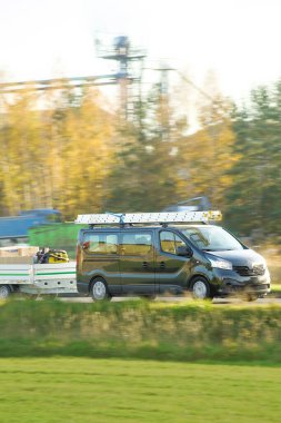 Kırsal yolda siyah minibüs römork çekiyor.