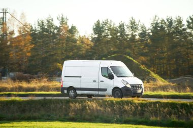 Ağaçlı kırsal yolda beyaz bir minibüs.