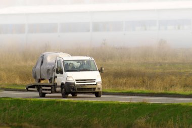 Beyaz kamyonet sisli kırsalda üstü kapalı araba taşıyor.