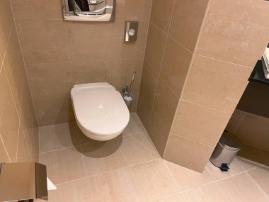 Modern fayanslı banyoda duvara asılmış parlak bir tuvalet.