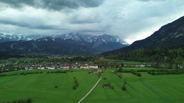 İlkbaharda dramatik bulutlu gökyüzünün altında karla kaplanmış görkemli Bavyera Alpleri