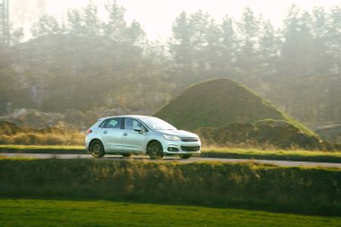 Günümüz hatchback 'i ağaçların yakınındaki bir yolda güneşli bir günde araba sürüyor.