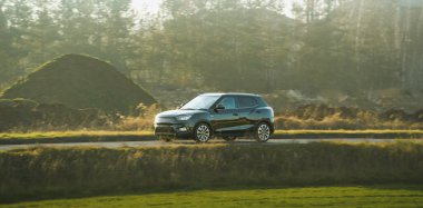 Siyah araba boş köy yolunda ilerliyor.