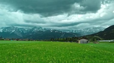 Ahırları ve fırtınalı gökyüzü olan Alp kırsalları