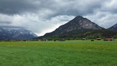 Bulutların altındaki çayırlarda ahşap barakalar.