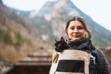 Kadın ve kara kedi birlikte dağ yolunda yürüyorlar.
