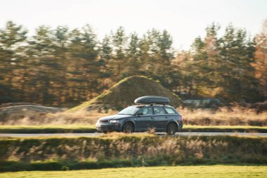 Gündüz vakti kırsal yolda giden siyah bir araba.