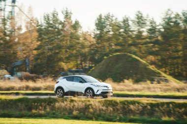 Beyaz hatchback sanayi bölgesini ve tarlaları geçiyor