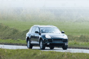 Lüks SUV ağaçların ve çimenli arazinin yanından geçiyor.