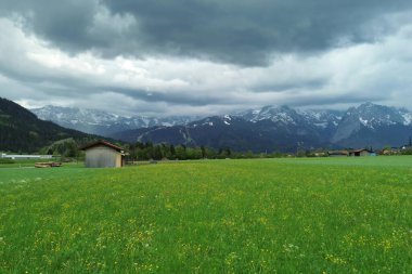 Ahşap ahırlar ve bulutlu gökyüzü ile Alp Vadisi