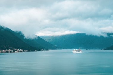 Bulutlu havada yeşil dağı geçen bir gemi.
