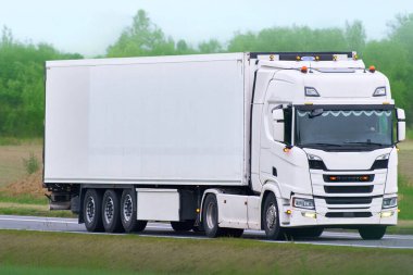 Beyaz lojistik kamyonu açık doğada sürüyor.