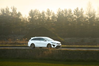 Kırsal yolda beyaz spor araba sürüyor.