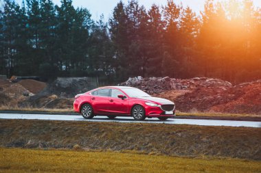 Kırmızı sedan orman yakınlarındaki ıslak yolda gidiyor.