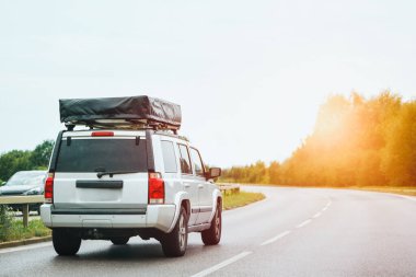 Çatı arası uyku çadırı olan bir SUV yolda ilerliyor.