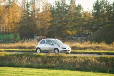 Beyaz hatchback sanayi bölgesini ve tarlaları geçiyor