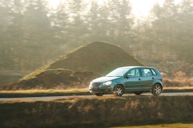 Siyah araba boş köy yolunda ilerliyor.