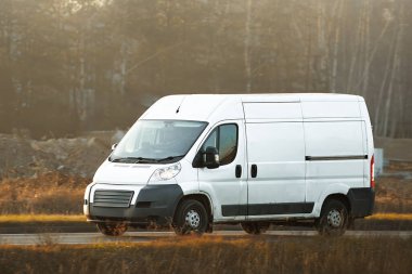 Beyaz minibüs doğada asfalt yolda ilerliyor.