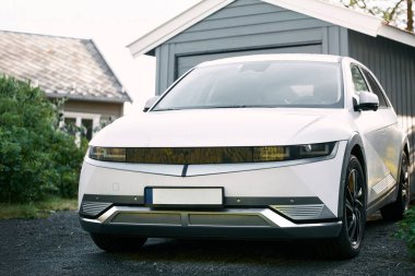 Gri bir garajın önüne park edilmiş beyaz elektrikli araba.