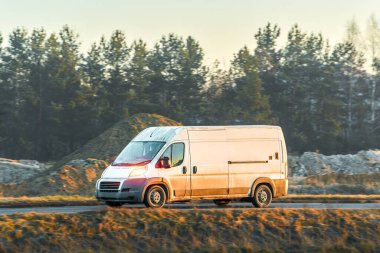 Büyük beyaz bir minibüs yolda mal taşıyor.