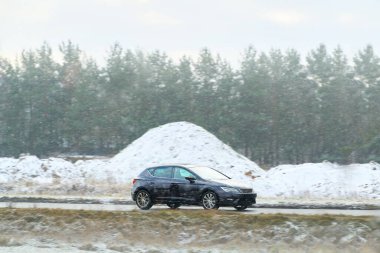 Karlı kış yolunda küçük bir araba sürüyor.
