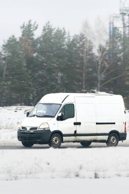 Karlı havada beyaz minibüs sürüyor.