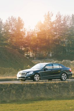 Tarz sahibi siyah bir sedan taşrada sürüyor.